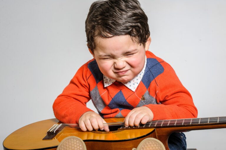 Boy leaning on an acoustic guitar in a studio portrait