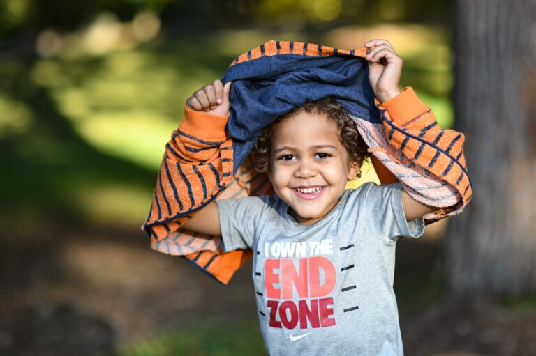 Child in an orange hoodie lifting their arms outdoors