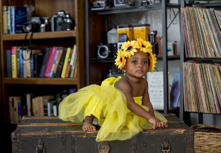 Woman in a yellow headwrap seated beside a bookshelf