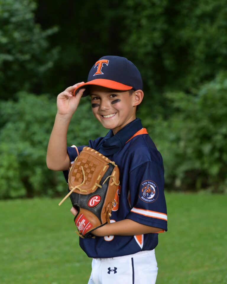 Boy posing outdoors with a baseball cap and glove