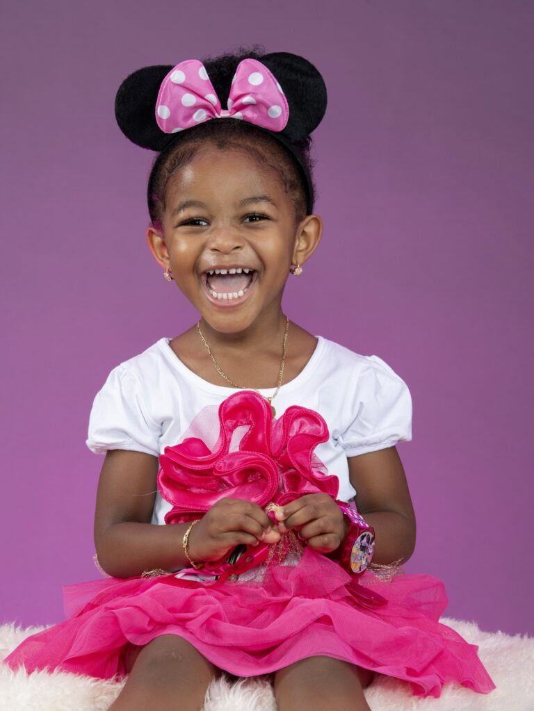 Smiling girl in a pink outfit with a Minnie-style bow in a studio portrait