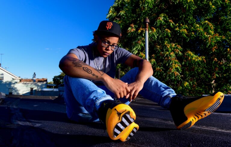 Man seated outdoors in blue attire and yellow shoes in a styled portrait