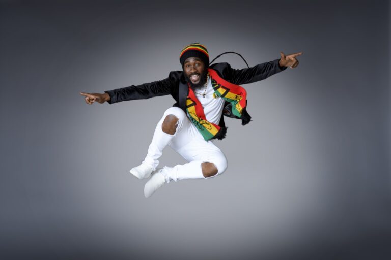 Man in a white outfit and rainbow vest jumping in a studio