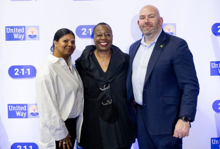 Three attendees at a nonprofit event backdrop marked 211