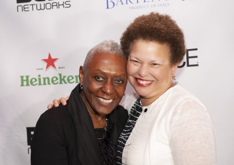 Two women posing at a branded reception backdrop