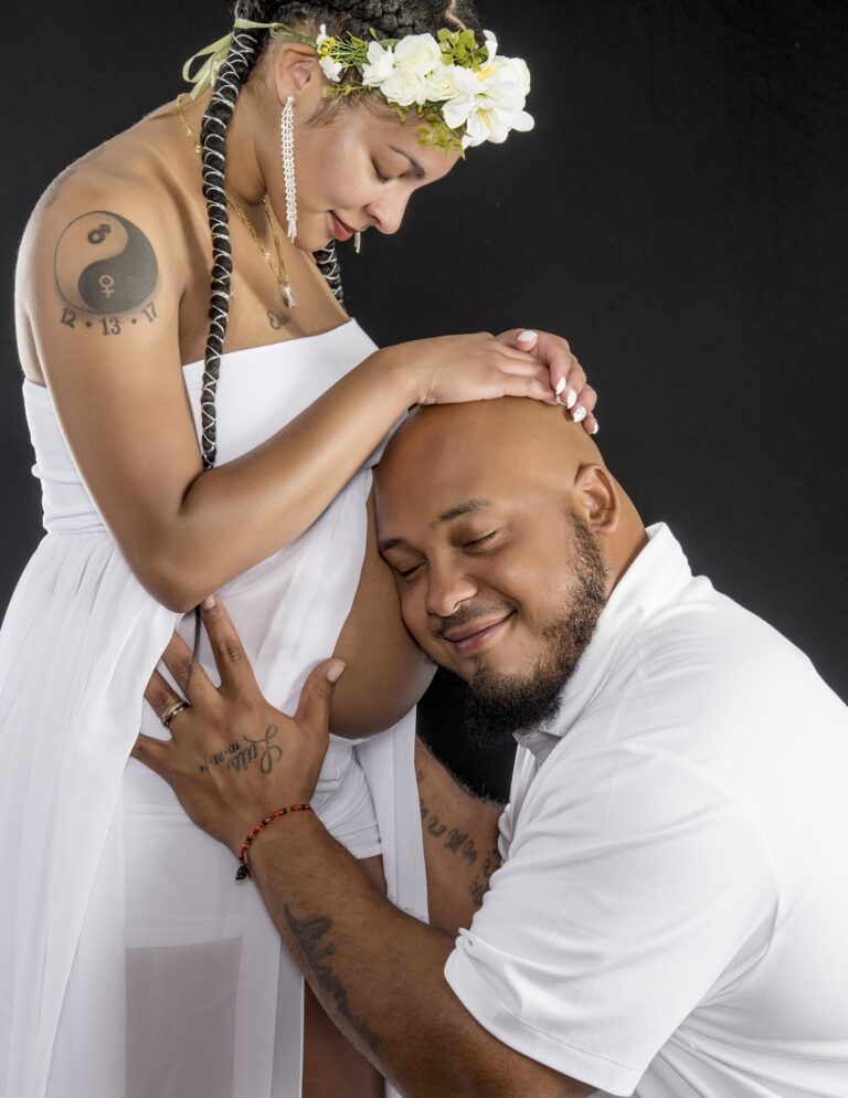 Expectant couple in white outfits posing in a studio