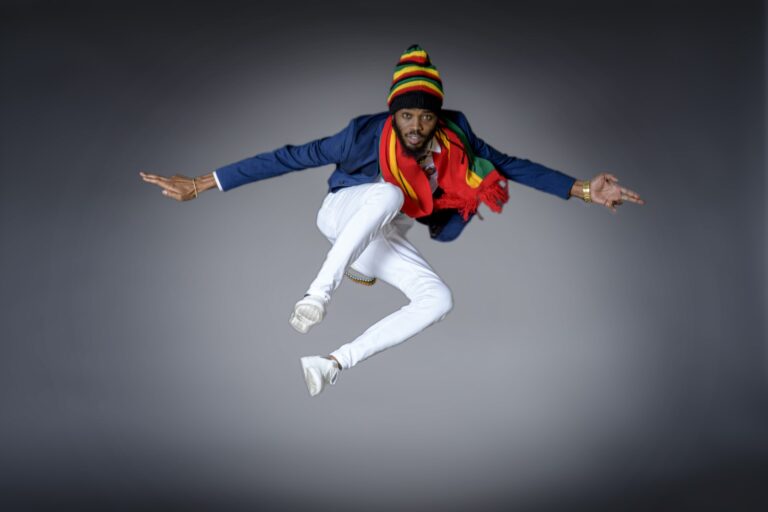 Man in blue and white clothing and a rainbow cap jumping in a studio