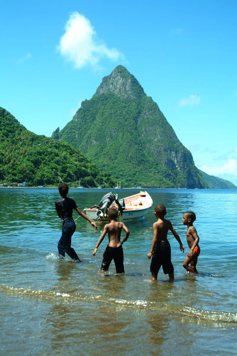 People standing in shallow water beneath coastal mountains