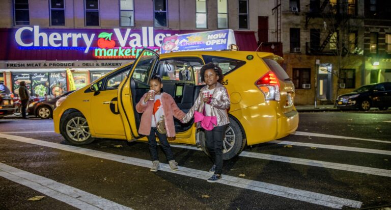 Yellow taxi at night on a city street with people