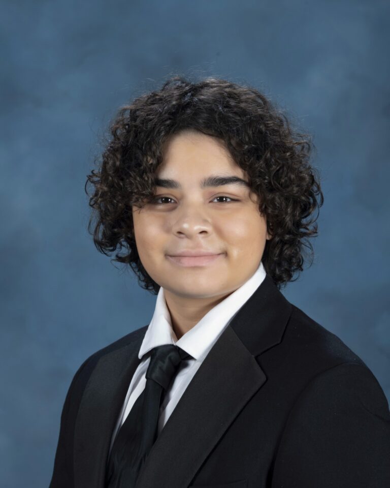 Young subject in dark suit and black tie, blue background