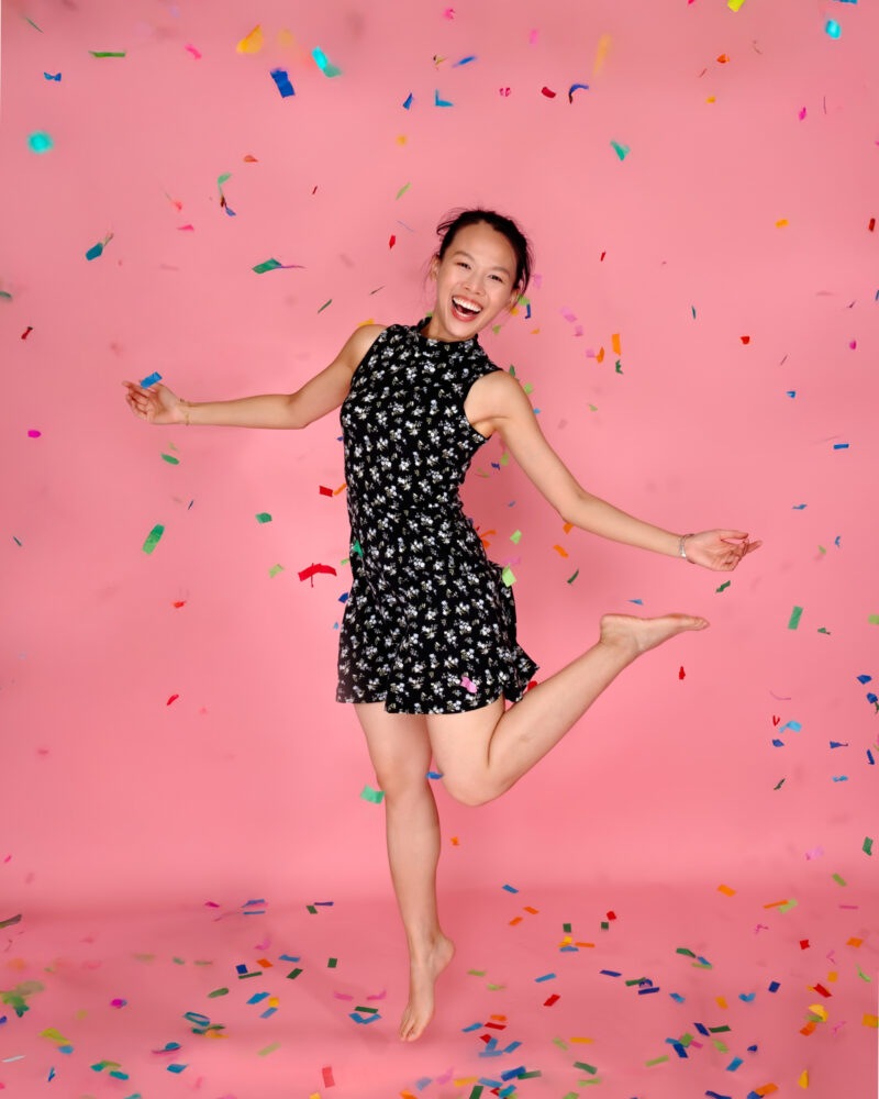 Jumping birthday portrait with colorful confetti against a pink studio backdrop