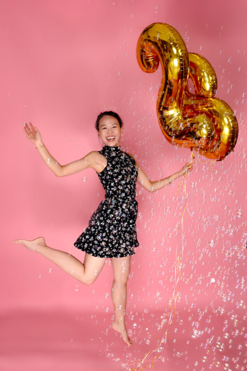 Jumping birthday portrait with bubbles and gold 28 balloons against a pink studio backdrop