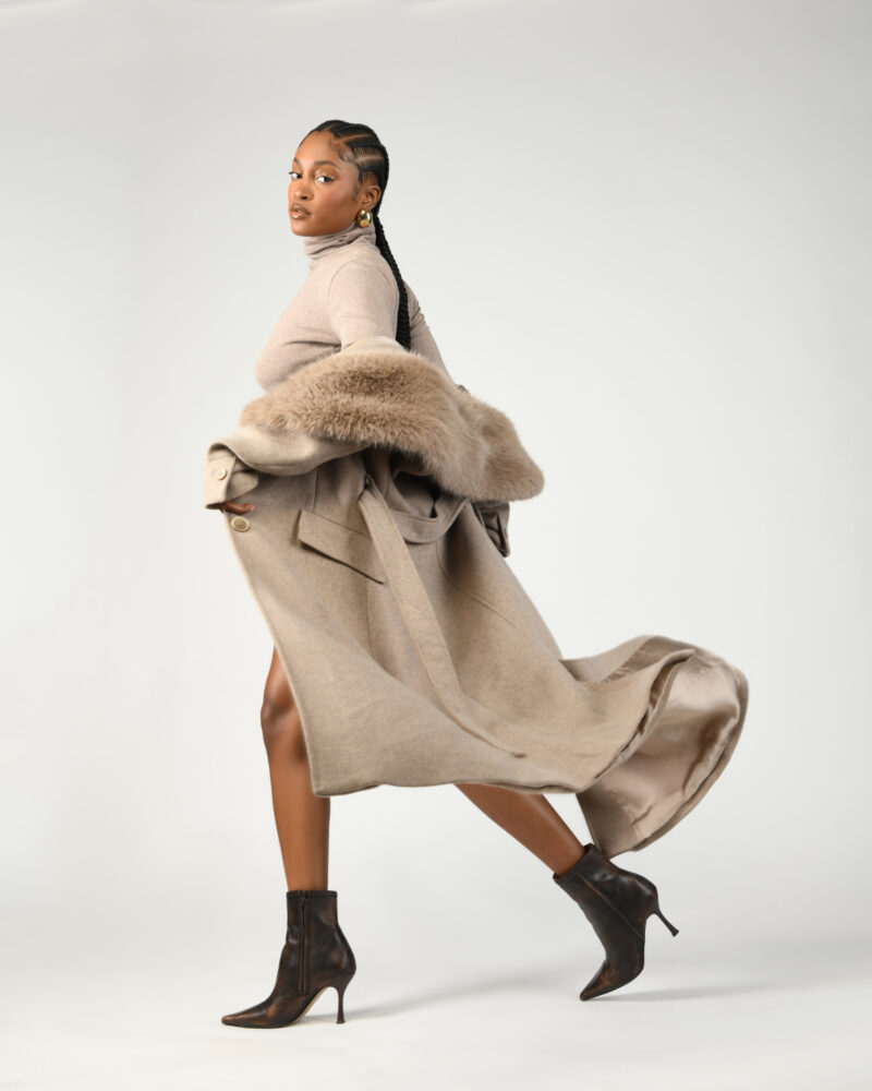 Studio fashion portrait in a flowing taupe coat against a light backdrop