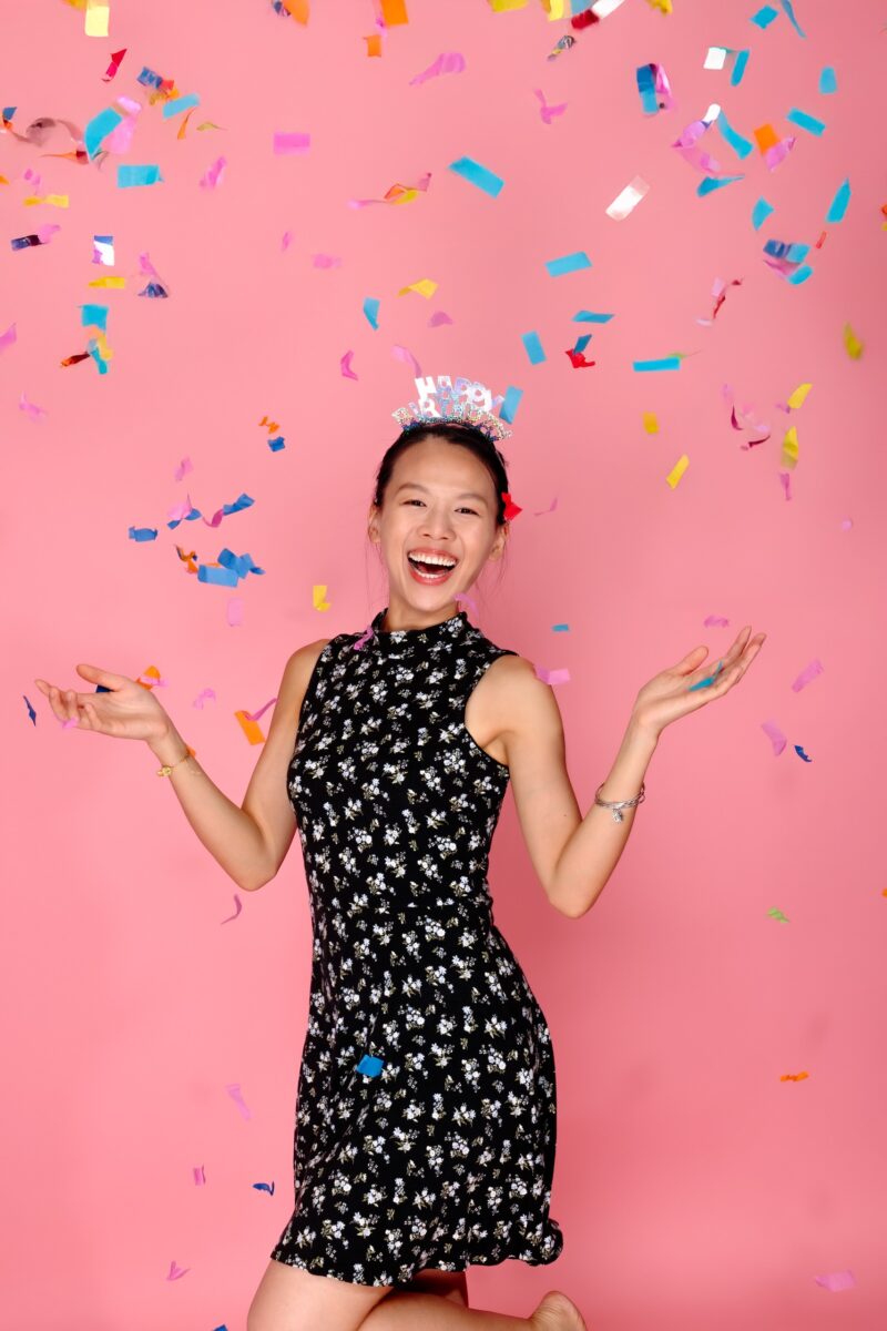 Laughing birthday portrait with colorful confetti against a pink studio backdrop