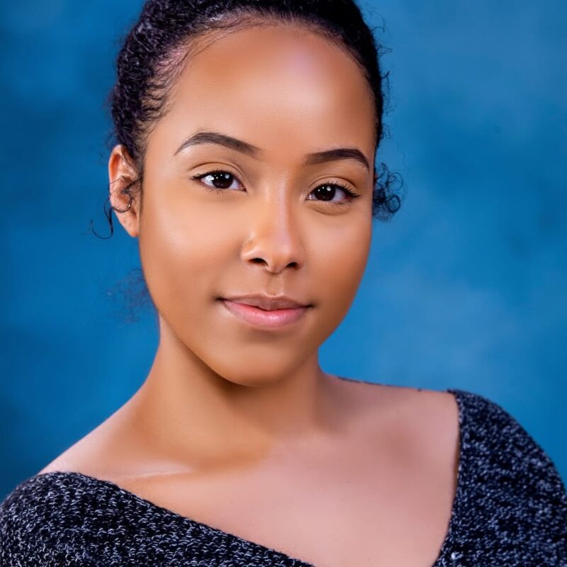 Headshot of a woman in a black top against a blue studio backdrop