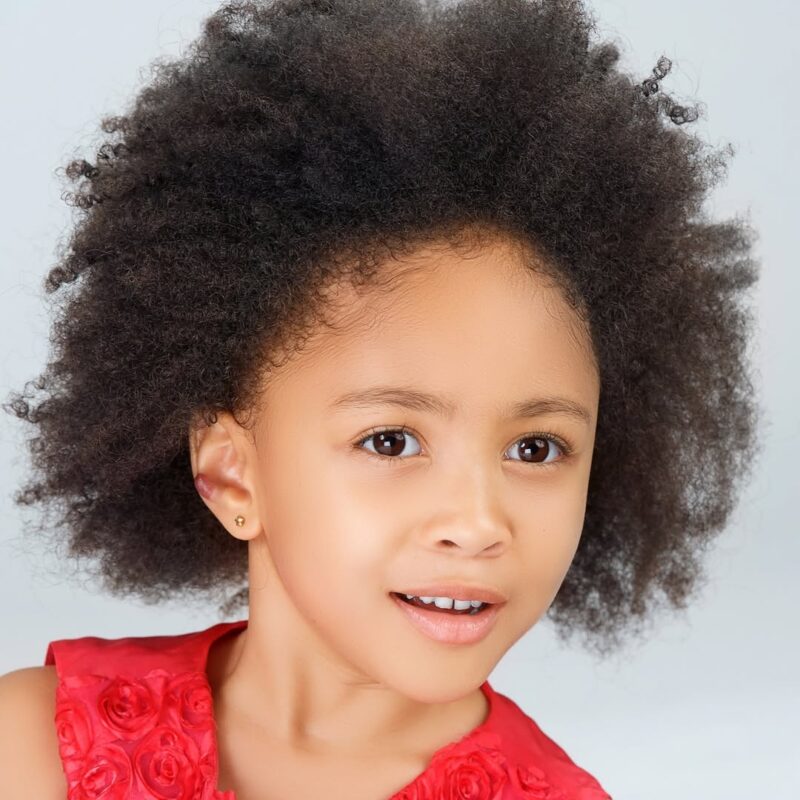 Studio portrait of a smiling child with curly hair in a red top