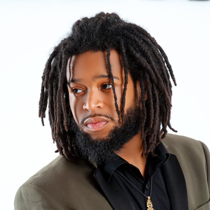 Studio headshot of a man with locs against a white background