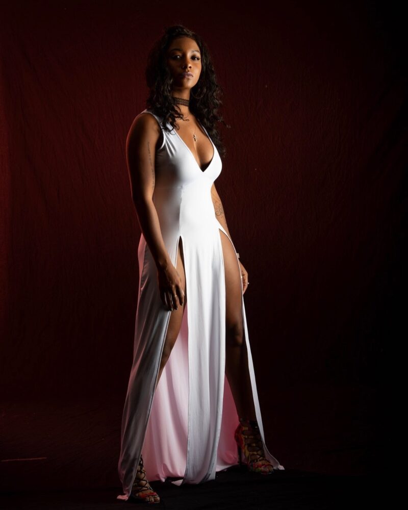 Dramatically lit studio portrait in a white gown against a dark red backdrop