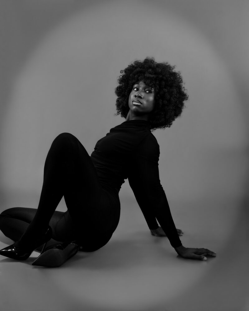 Seated monochrome studio portrait with one hand on the floor