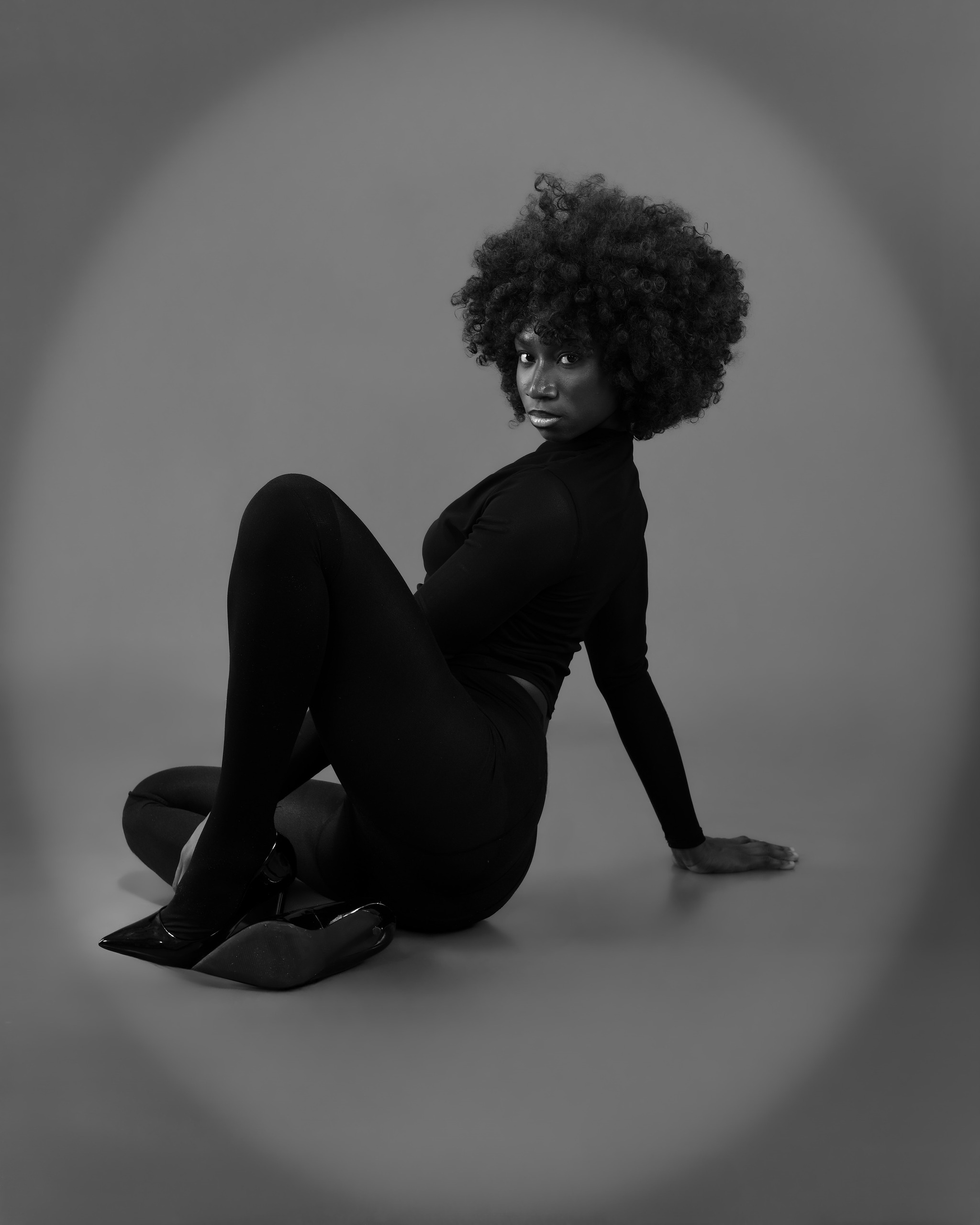 Seated monochrome studio portrait against a circular spotlight