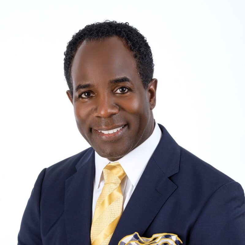 Professional headshot of a smiling man in a navy suit and yellow tie