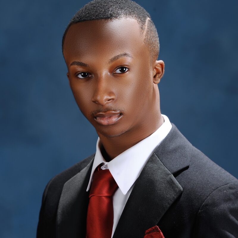 Studio headshot in a dark suit and red tie against a blue backdrop