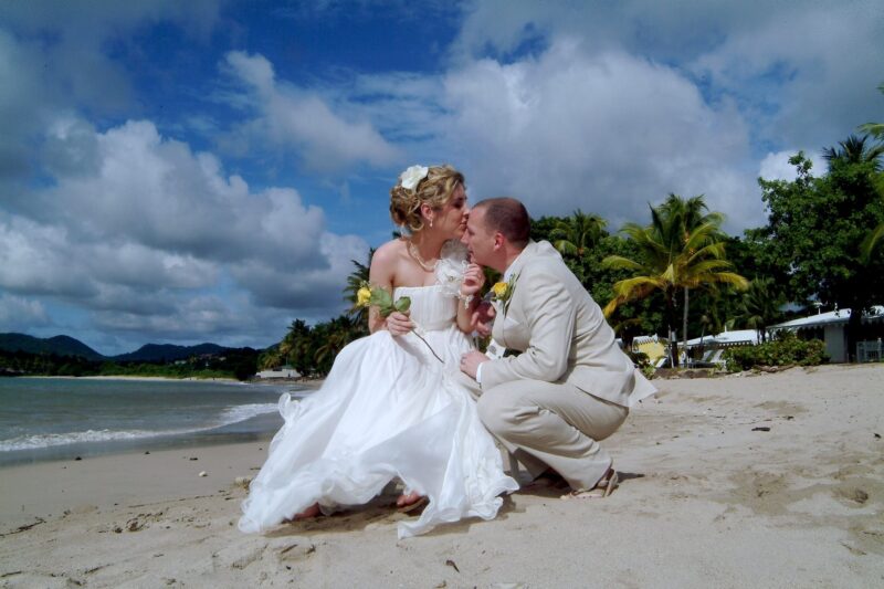 Bride and groom sharing a kiss on a tropical beach beneath a cloud-filled sky