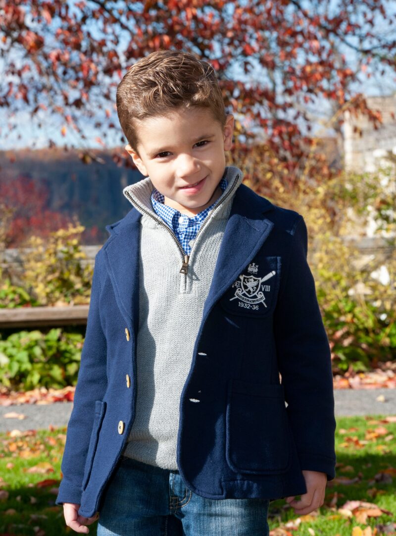 Child in a navy suit standing outdoors among autumn leaves