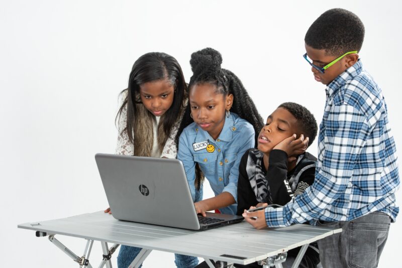 Four children gathered around a laptop against a white studio backdrop