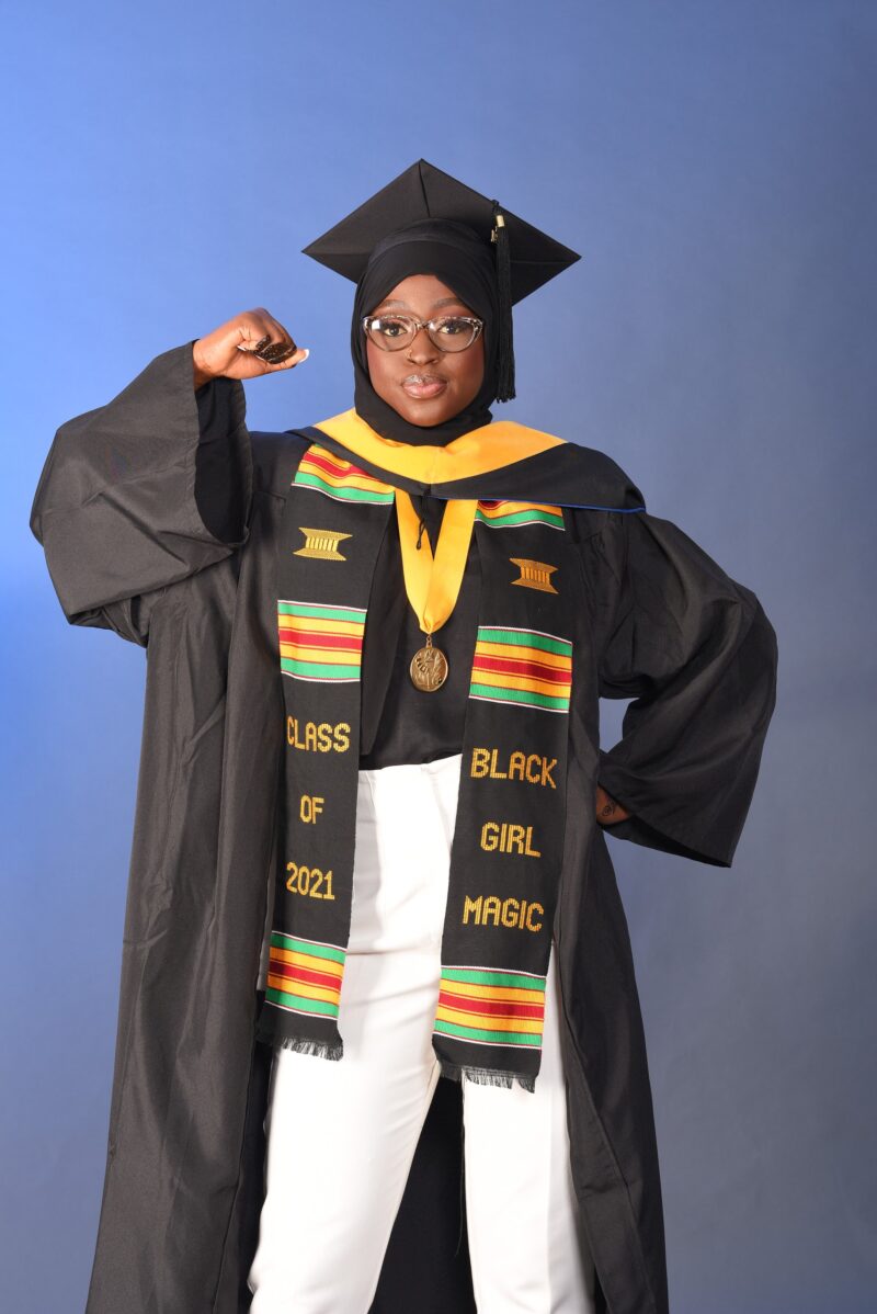 Graduate holding her cap while wearing a black gown and colorful graduation stoles