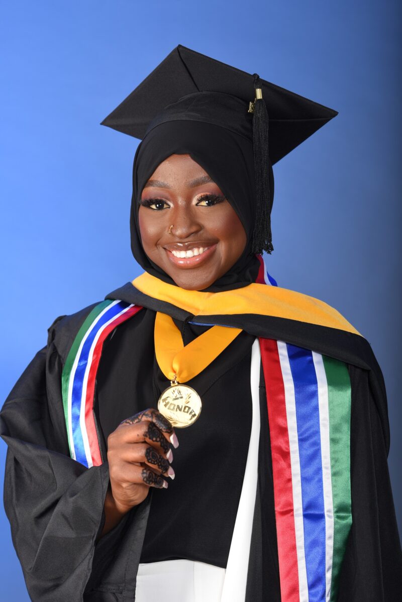 Smiling graduate holding a diploma in a black cap and gown with colorful stoles