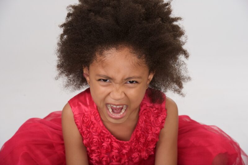 Playful studio portrait of a child leaning forward in a red dress