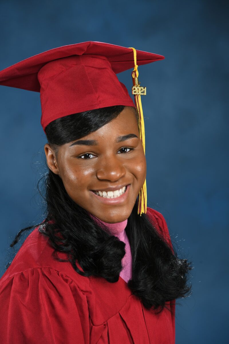 Smiling graduate in a red cap and gown in a close-up studio portrait