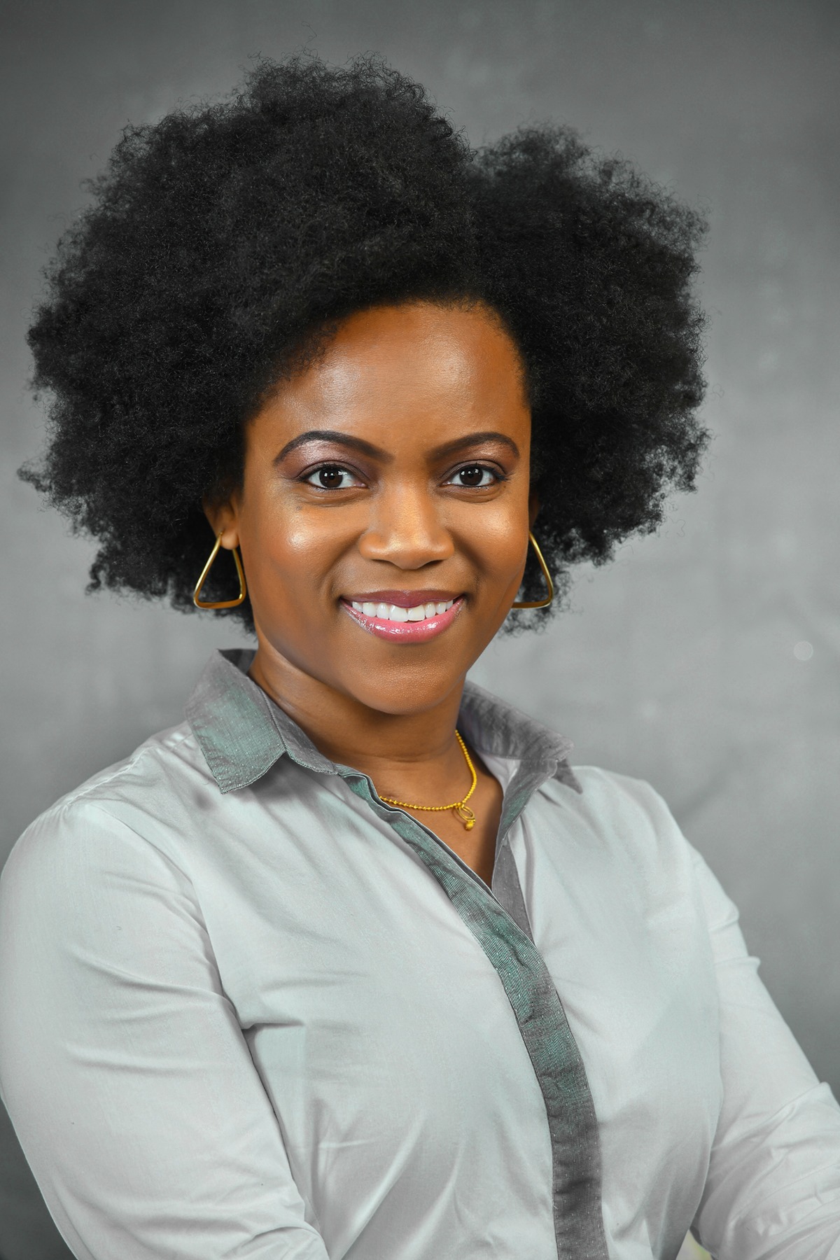 Smiling woman with natural curly hair wearing a gray blouse against a gray studio backdrop