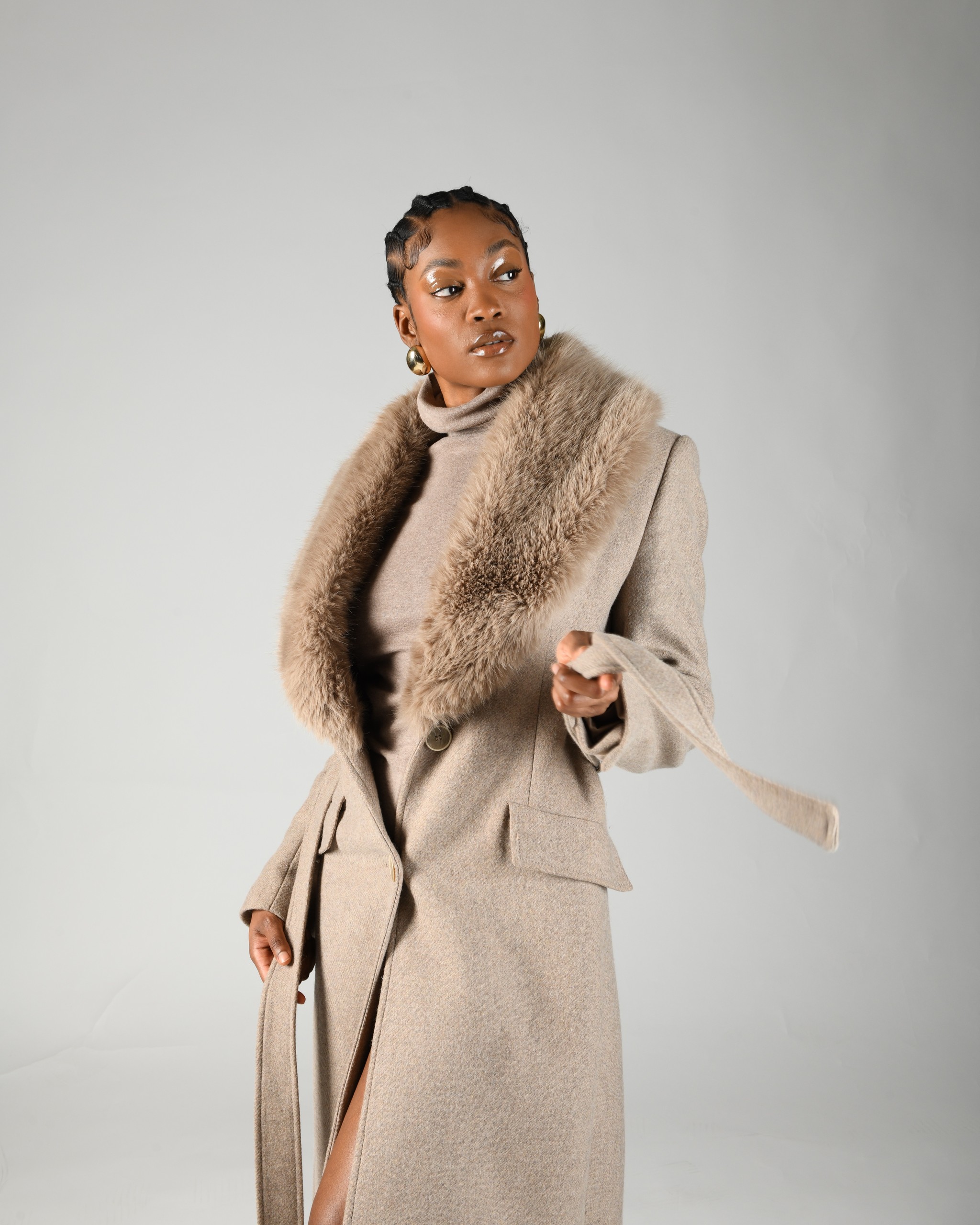 Studio fashion portrait of a woman holding a taupe coat with a textured collar